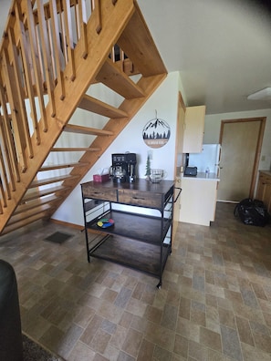 A kitchen with a wooden staircase, a coffee station, and a wall-mounted sign. - Bluff Point Hideaway Private & Cozy 2 Bedroom Cabin (Keuka Park)