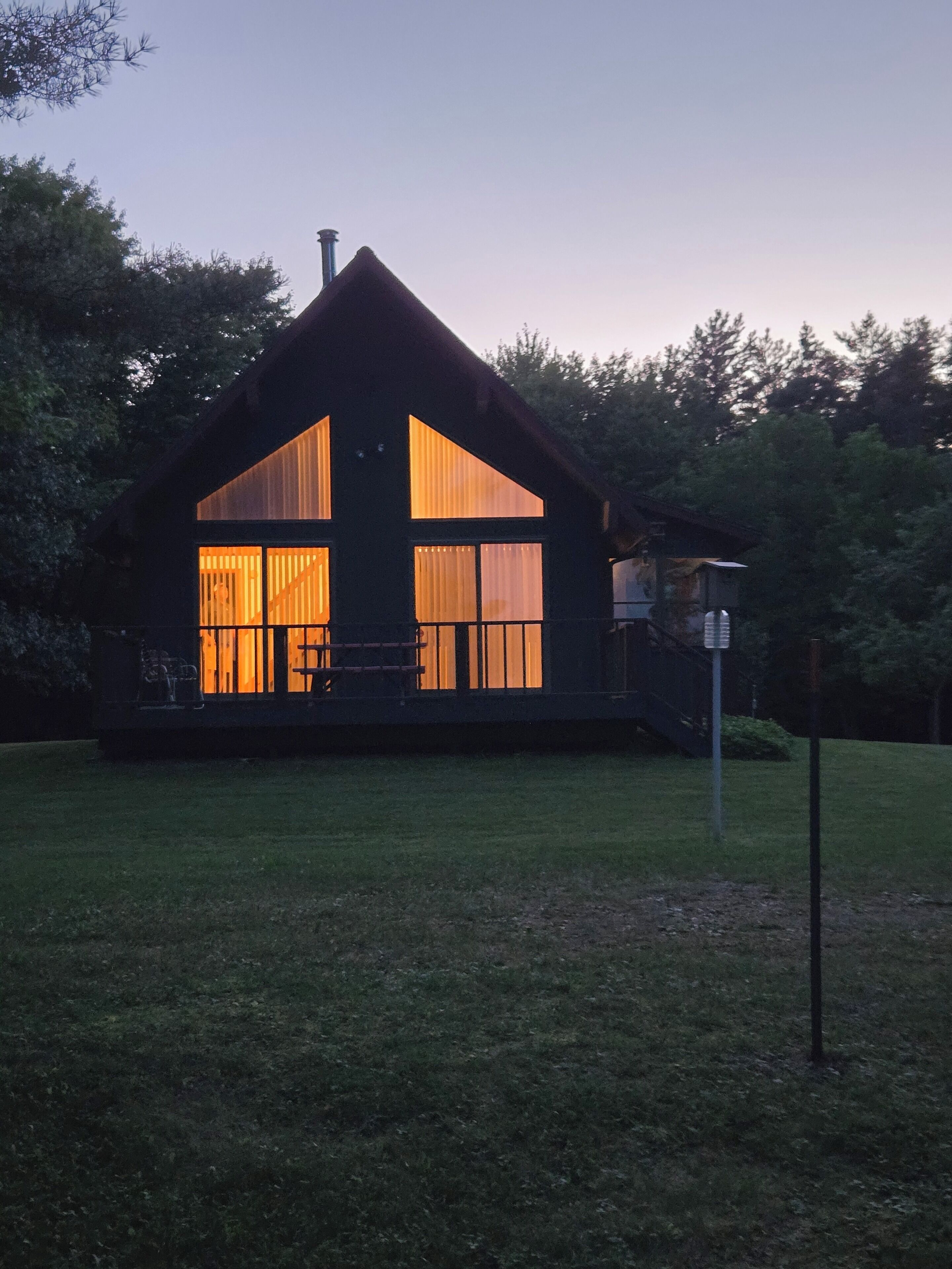 Une cabane à deux étages dotée de grandes fenêtres et d’un porche couvert.