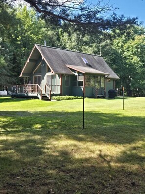 A single-story building with a porch, a small deck, and a grassy yard. - Bluff Point Hideaway Private & Cozy 2 Bedroom Cabin (Keuka Park)