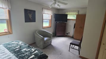 Un dormitorio con cama, una silla, televisor, armario y ventilador de techo.