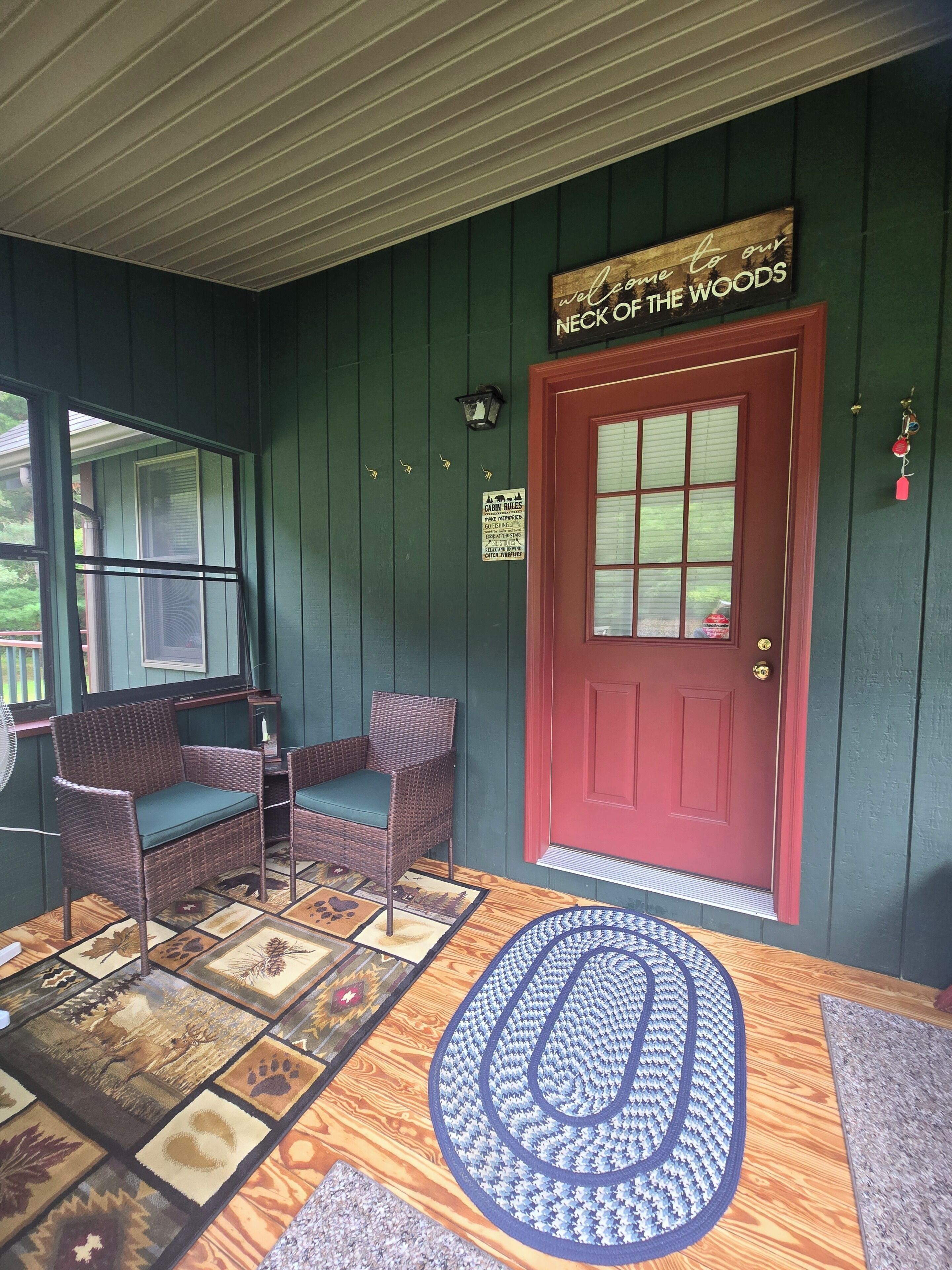 A porch with wicker furniture, a red door, and a welcome sign.