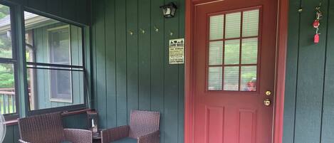 A porch with wicker furniture, a red door, and a welcome sign.