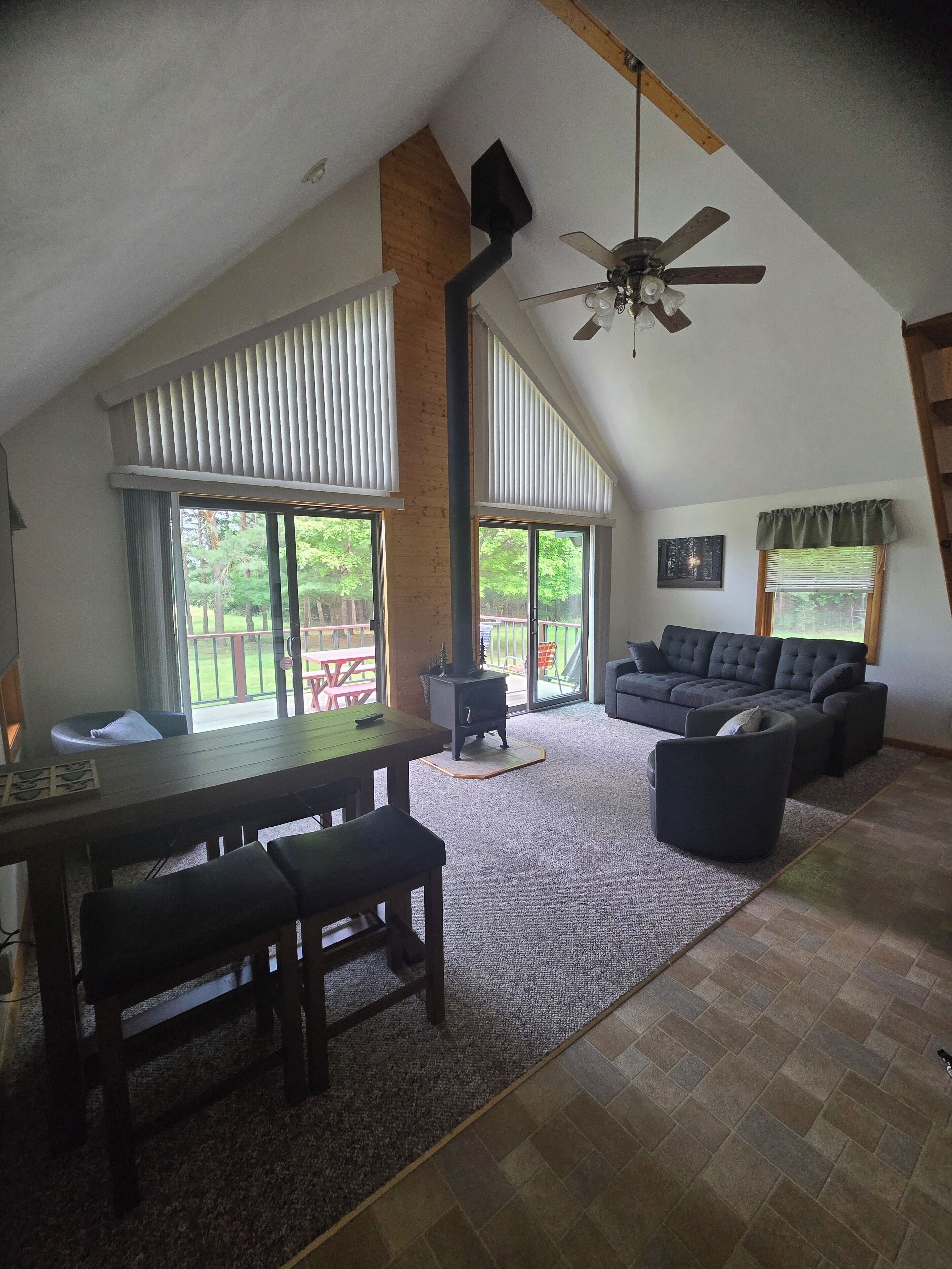 A spacious living area with a high ceiling, a fireplace, a sofa, and a dining table with chairs.