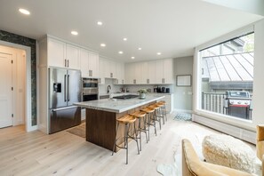 A modern kitchen with white cabinetry, stainless steel appliances, and a central island with bar stools. - Designer Pinnacle Home with Free DV Shuttle (Park City)
