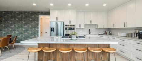 A modern kitchen with white cabinetry, a marble countertop, and a central island with bar stools.