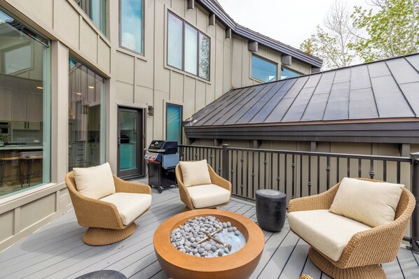 Eine Terrasse mit Korbmöbeln und einem Feuerkorb, mit Blick auf ein Gebäude mit großen Fenstern und einer Küchenzeile.