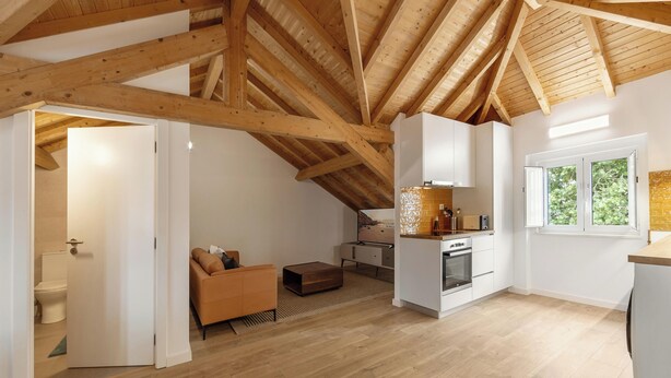 Una habitación moderna estilo loft con vigas de madera a la vista, kitchenette, sofá y ventana con vistas.