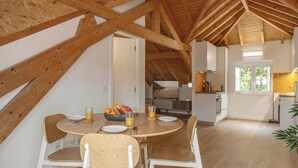 Un comedor con una mesa y sillas de madera, una cocina al fondo y un techo alto con vigas a la vista.