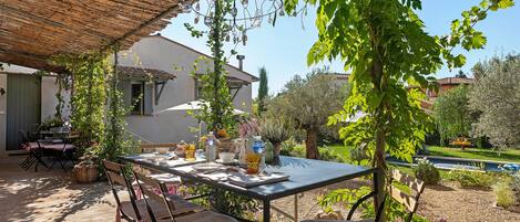 Un área de comedor al aire libre con una mesa lista para dos personas, rodeada de sillas, bajo un techo de paja.