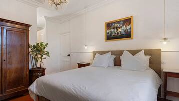 Una camera d'albergo con un letto grande, un armadio in legno, una pianta in vaso, un quadro appeso al muro e un lampadario.