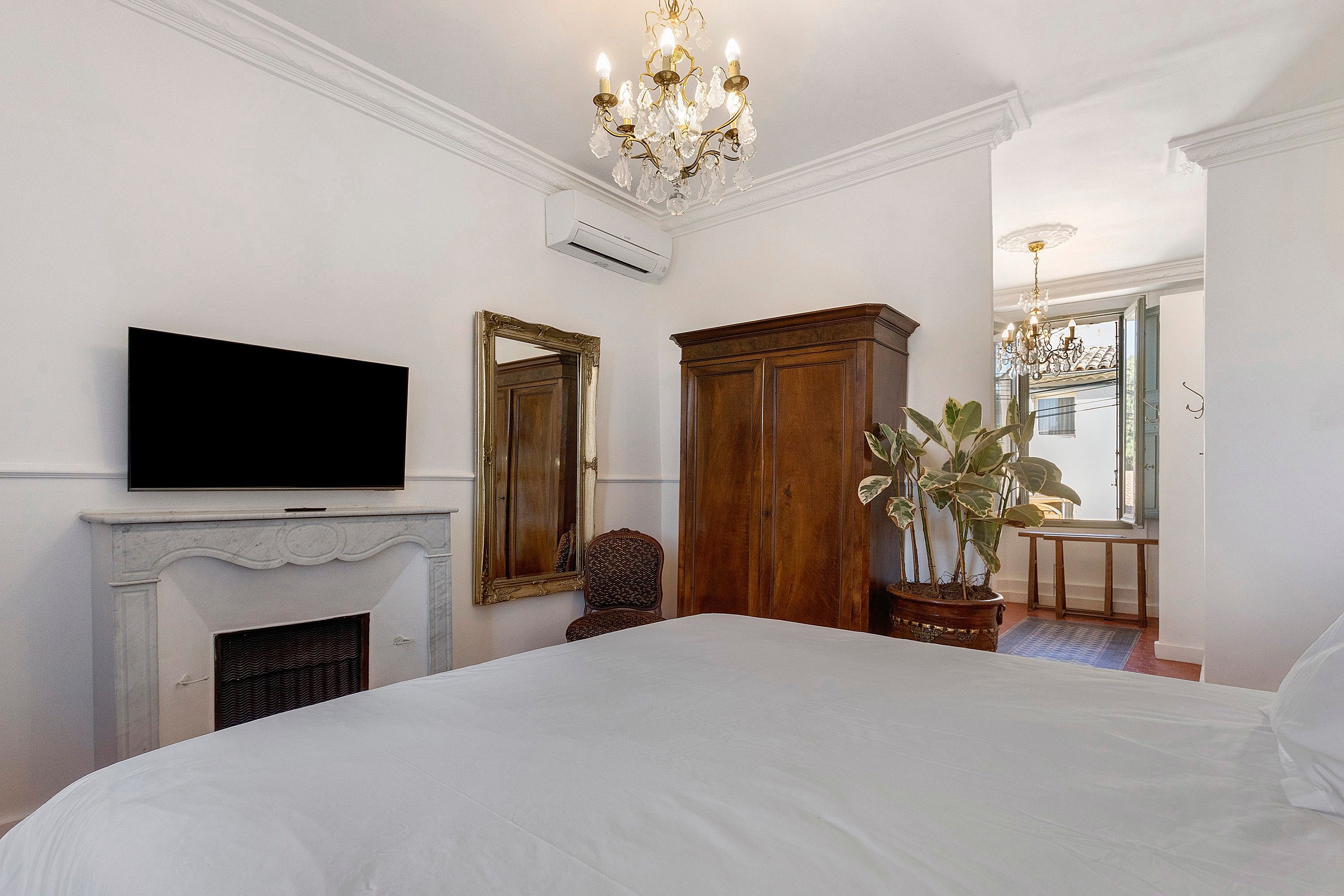 Habitación de hotel con una cama grande, televisión, chimenea, espejo, armario y una planta en maceta.