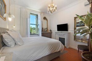 Quarto com cama grande, televisão, lareira e janela com cortinas.