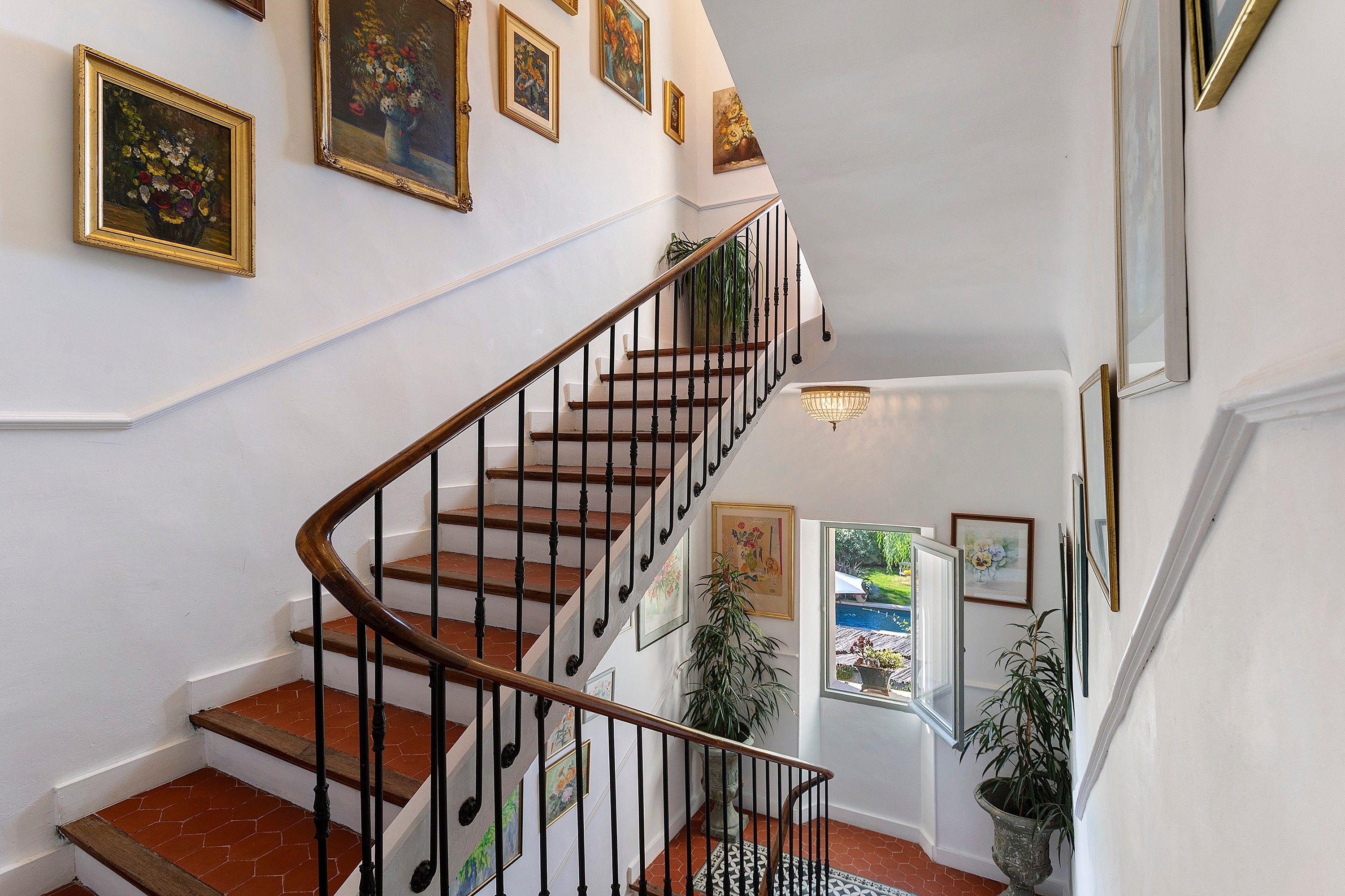 A staircase with a wooden handrail and black balusters, leading to an upper level with a view of a pool.