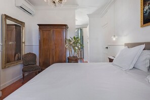 Un dormitorio con una cama grande, un armario de madera, una silla, una planta en maceta y un espejo.