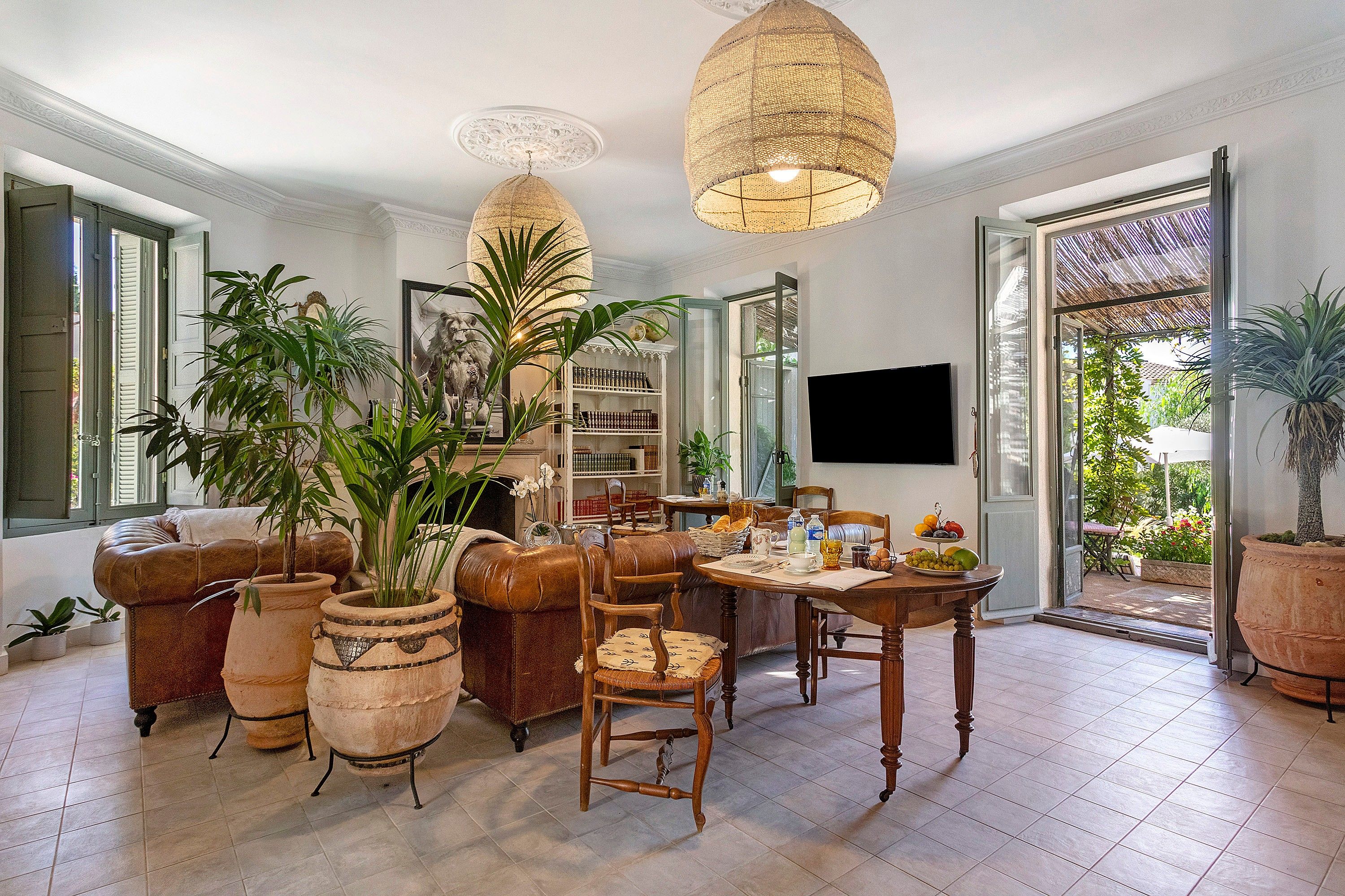 A spacious living room with a fireplace, a dining area with a table set for two, and a large window with a view of greenery.