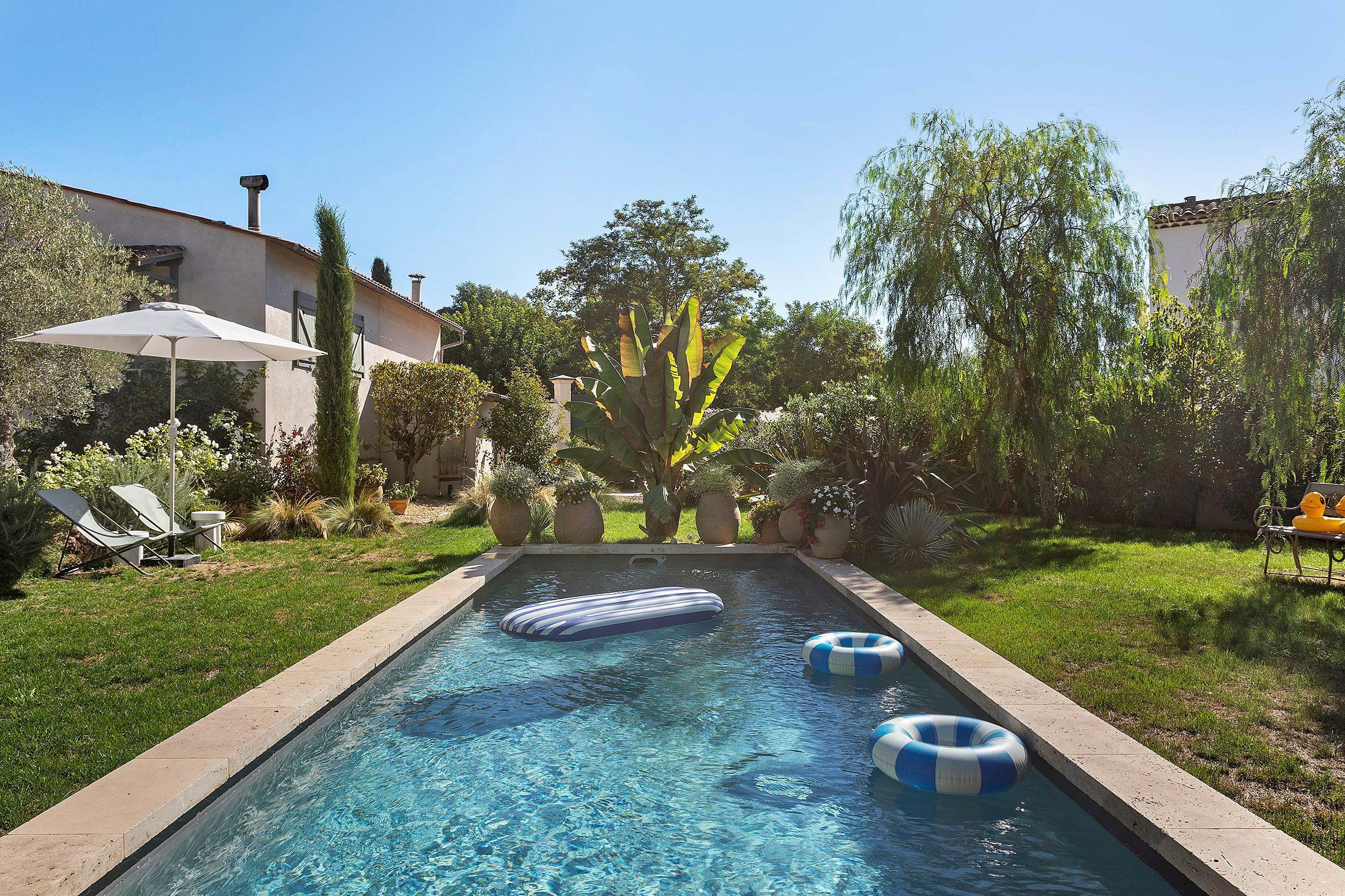 Una piscina con flotadores, rodeada de césped y plantas en macetas.