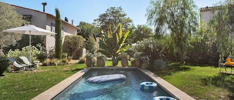 Una piscina con flotadores, rodeada de césped y plantas en macetas.