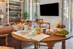 A dining area with a wooden table set for breakfast, including bread, eggs, and fruit.
