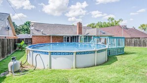 Ein Garten mit Swimmingpool, einer Holzterrasse und einem Ziegelhaus.