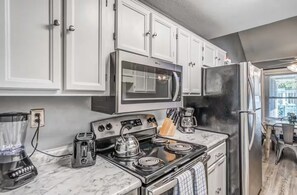 A kitchen with white cabinets, a microwave, a stove, and a refrigerator.