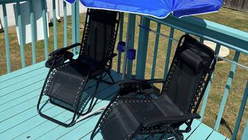 Un parasol bleu offre de l’ombre sur deux chaises longues noires, qui sont placées sur une terrasse turquoise.