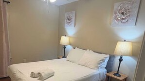 Ein Hotelzimmer mit einem Einzelbett, zwei Nachttischlampen, einem Deckenventilator und zwei floralen Wandbildern.