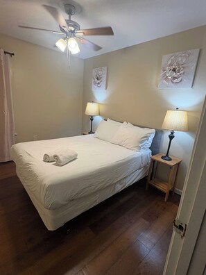 Ein Hotelzimmer mit einem Einzelbett, zwei Nachttischlampen, einem Deckenventilator und zwei floralen Wandbildern.