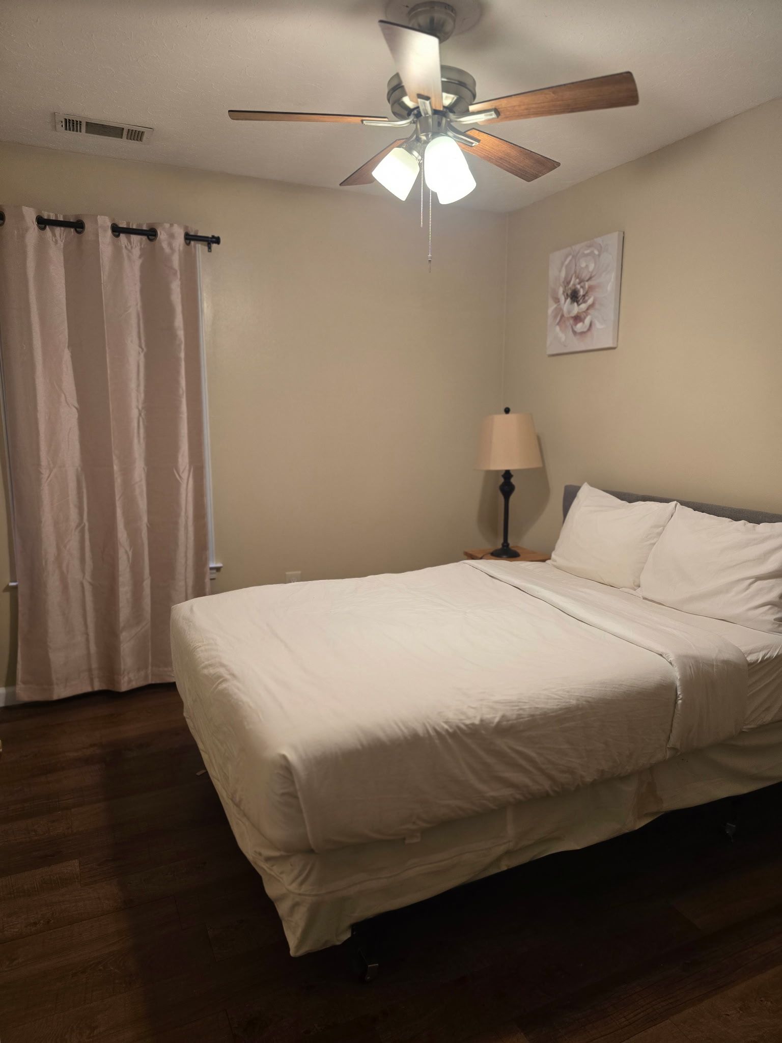 Une chambre d’hôtel avec un lit, un ventilateur de plafond, une table de chevet avec une lampe et une fenêtre avec des rideaux.