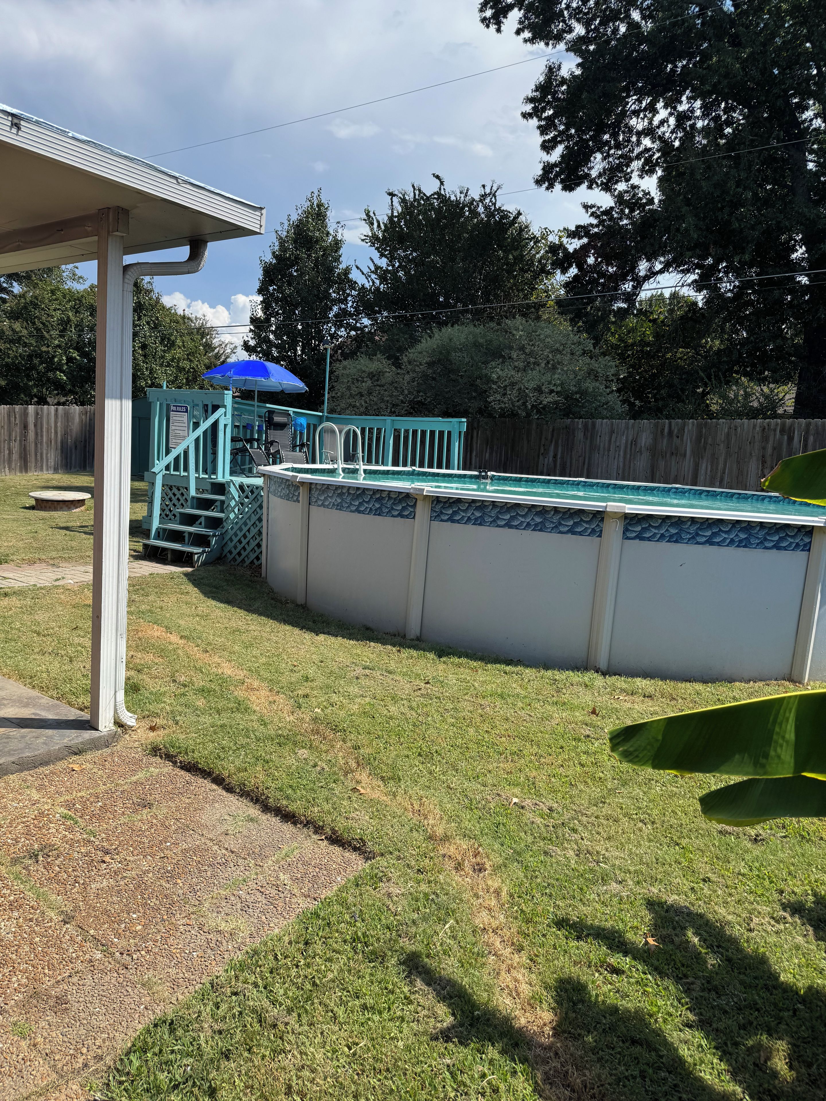 Un jardin avec une piscine, une terrasse couverte et une clôture en bois.