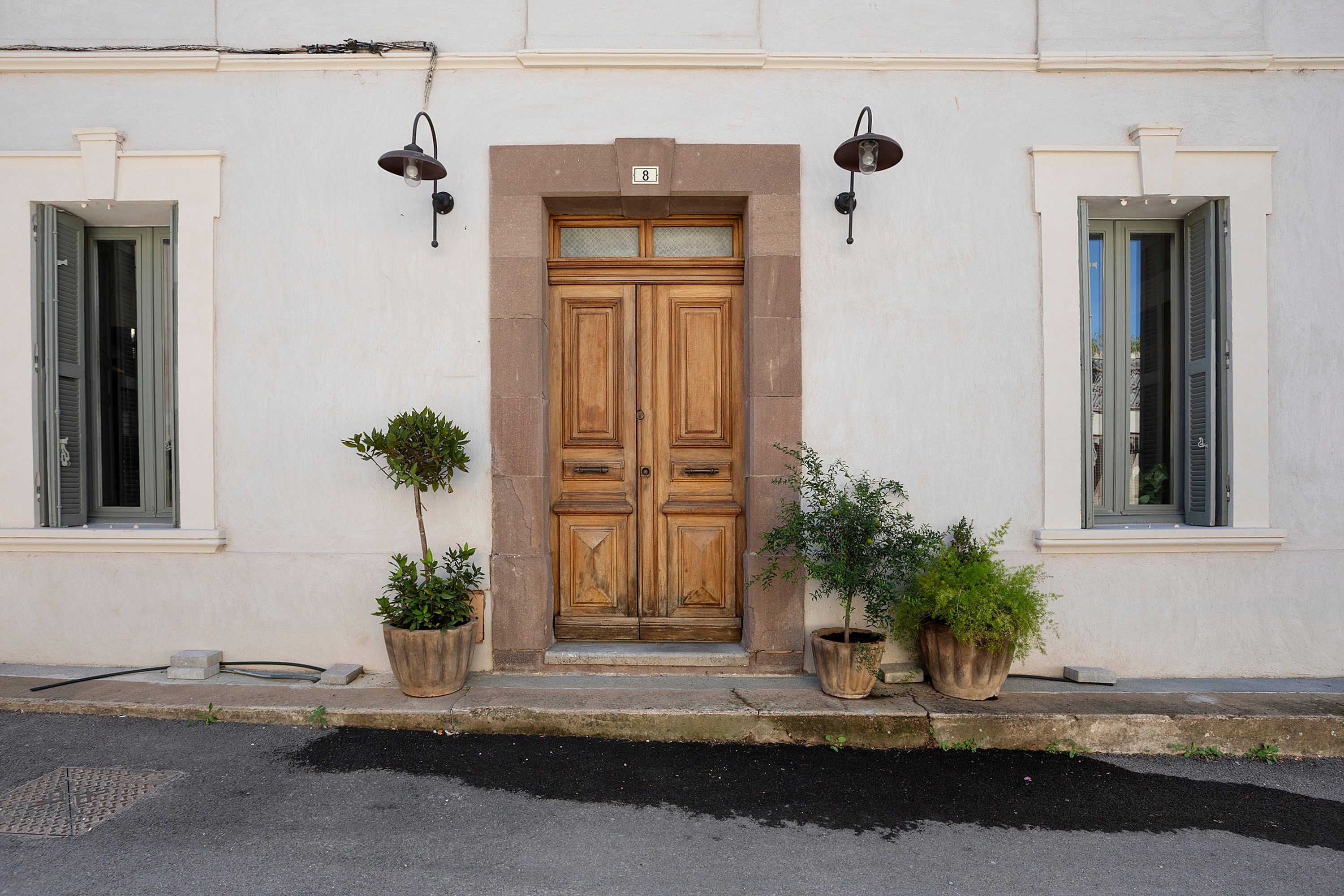 Un bâtiment doté d’une double porte en bois, de deux plantes en pot et de deux lampes fixées au mur.