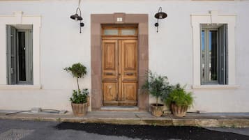 Un bâtiment doté d’une double porte en bois, de deux plantes en pot et de deux lampes fixées au mur.