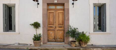 Un edificio con una puerta doble de madera, dos macetas y dos luces fijadas a la pared.