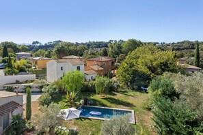 A residential area with a swimming pool, surrounded by greenery and houses with tiled roofs.