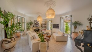 Ein geräumiges Wohnzimmer mit einer Sofagarnitur, einem Couchtisch und einem Kamin. Es befinden sich Blumentöpfe und ein Fernseher im Raum.