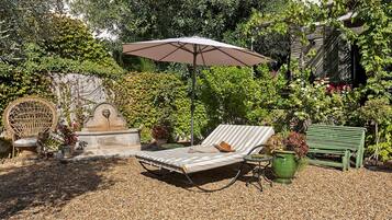 Un jardin avec un fauteuil de relaxation, une petite table, une plante en pot et une statue.