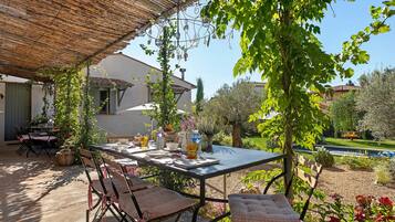 Un área de comedor al aire libre con una mesa lista para dos personas, rodeada de sillas, bajo un techo de paja.