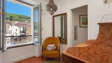 Une pièce avec vue sur la ville, visible par une fenêtre ouverte, comprenant une chaise, un miroir et un meuble en bois.