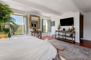 Une chambre à coucher comprenant un lit, un bureau, une chaise, un grand miroir, une télévision et une plante en pot.