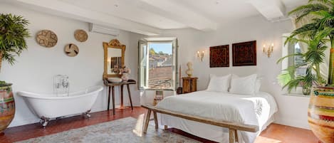 Un dormitorio con una cama grande, una bañera y un ventanal con vistas a edificios.