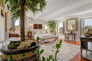 A spacious bedroom with a large bed, a sitting area with a table and chair, and a view of the outdoors through a large window. - Bed and Breakfast 'Chambre 6' with Shared Pool, Wi-Fi and Air Conditioning (La Motte)