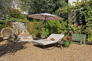 A garden with a lounge chair, a small table, a potted plant, and a statue.