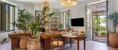 A spacious living room with a fireplace, a dining area with a table set for two, and a large window with a view of greenery.