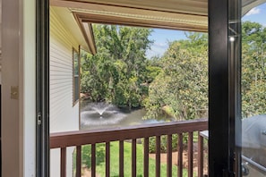 Blick von einem Balkon mit Holzgeländer auf einen Garten mit Wasserspiel und dichtem Grün.