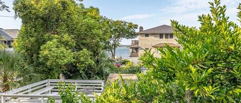 A coastal property with a wooden deck, lush greenery, and a view of the sea.
