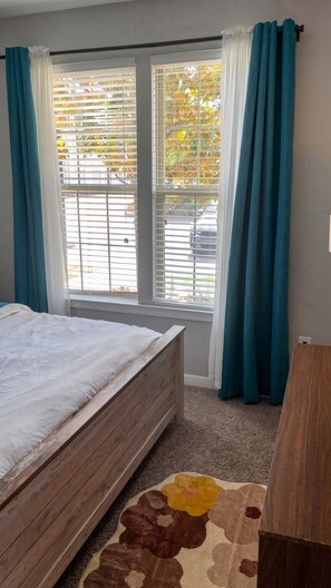 Ein Schlafzimmer mit Bett, einem Fenster mit Jalousien und Blick nach draußen.