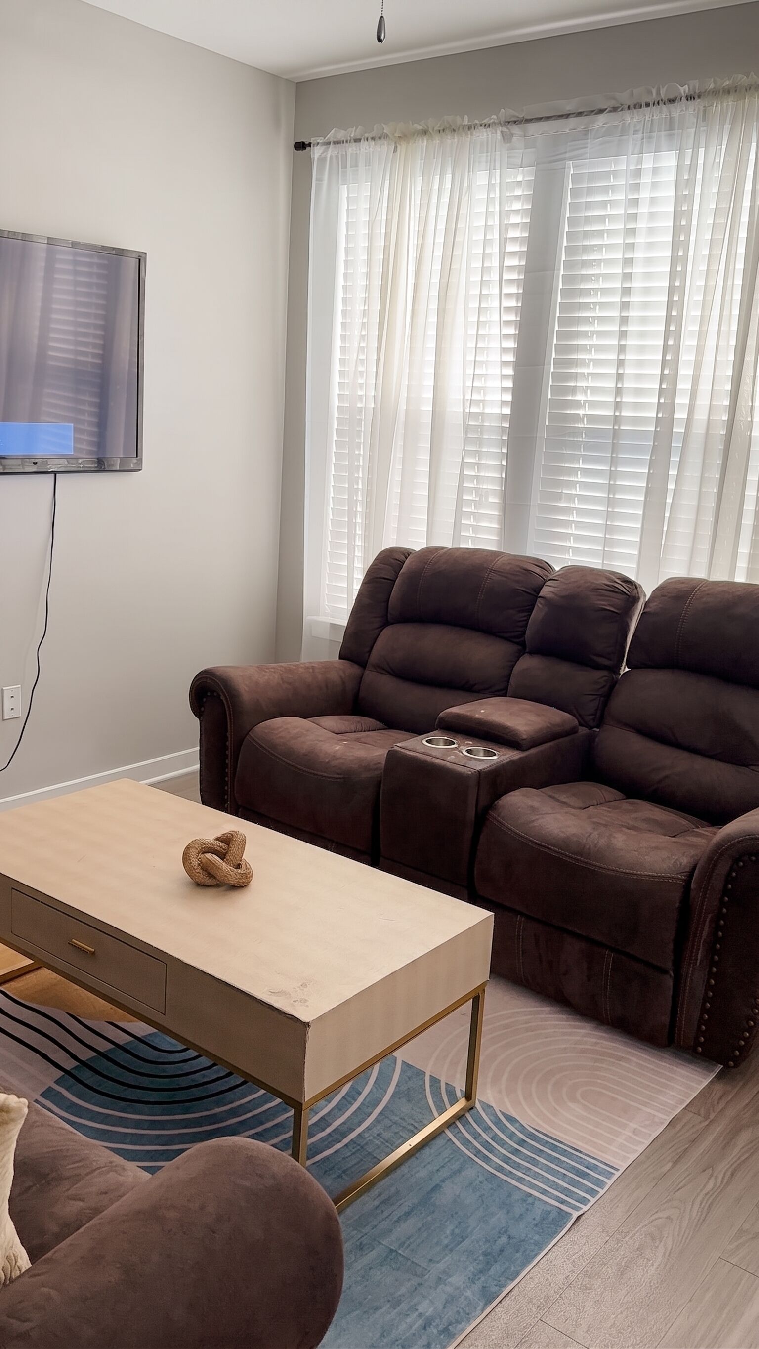 Ein Wohnzimmer mit einem braunen Sofa, einem Holztisch und einem an der Wand befestigten Fernseher.
