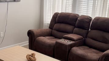 Ein Wohnzimmer mit einem braunen Sofa, einem Holztisch und einem an der Wand befestigten Fernseher.