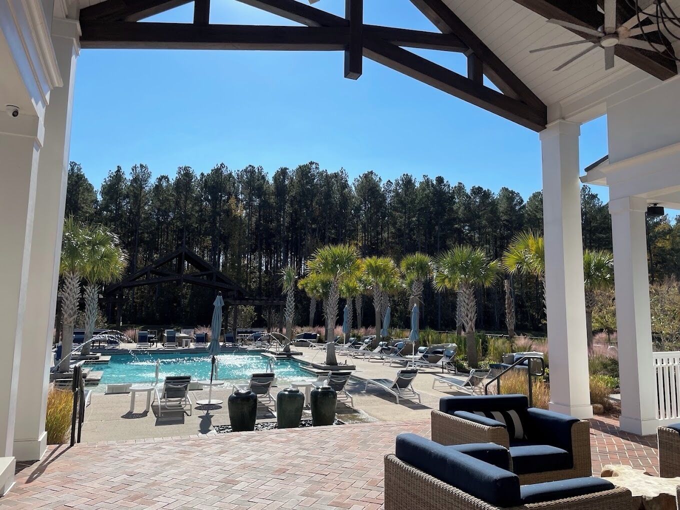 A covered outdoor pool area with lounge chairs and a view of a forested area.