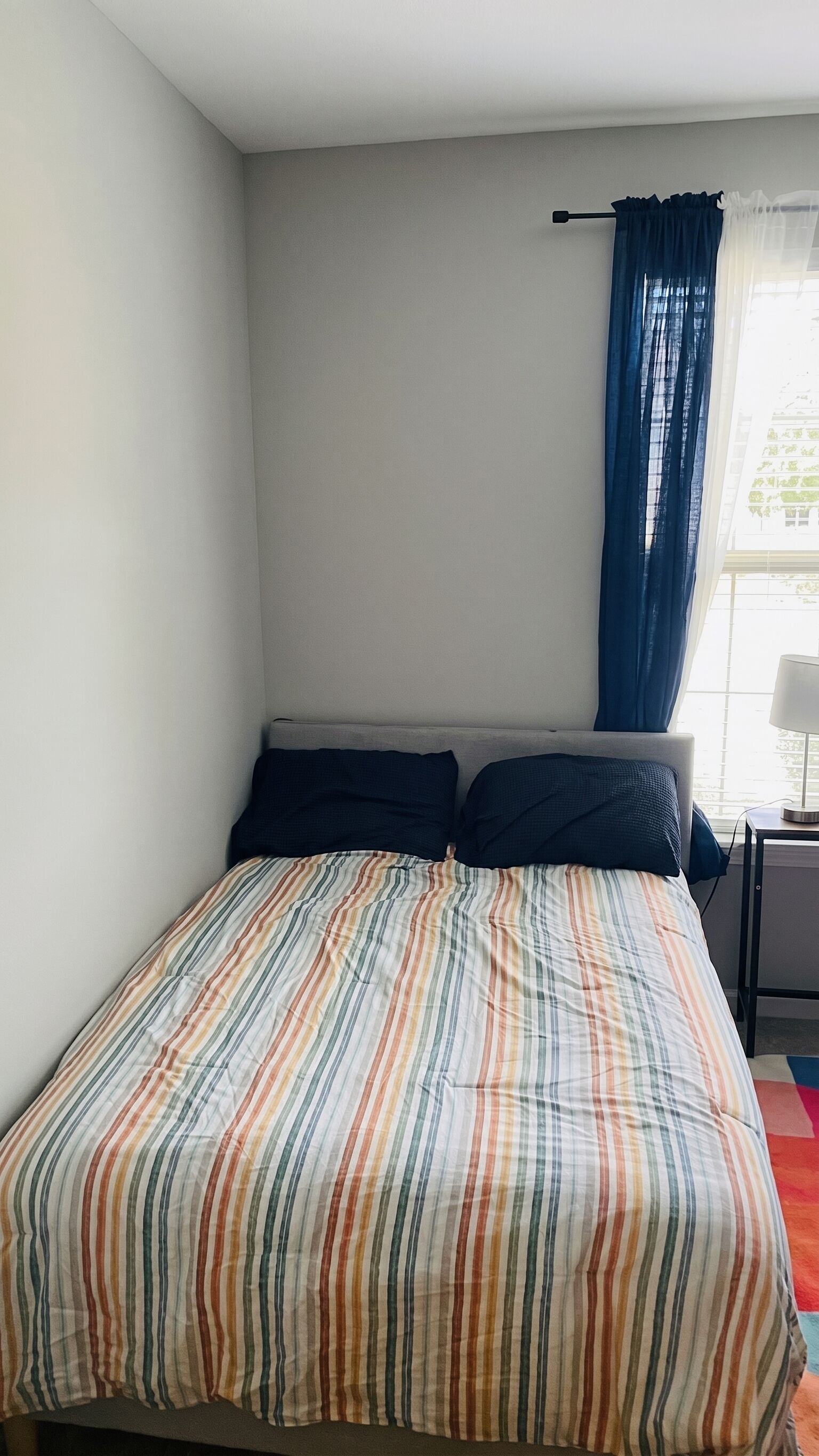 Una camera da letto con un letto, un comodino, una lampada e una finestra con tende.