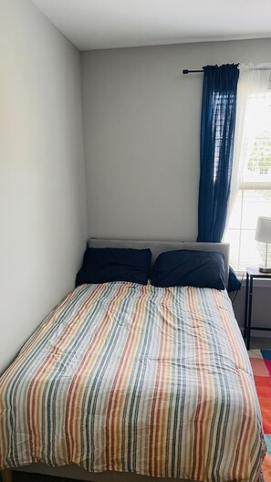 Une chambre à coucher avec un lit, une table de chevet, une lampe et une fenêtre avec des rideaux.